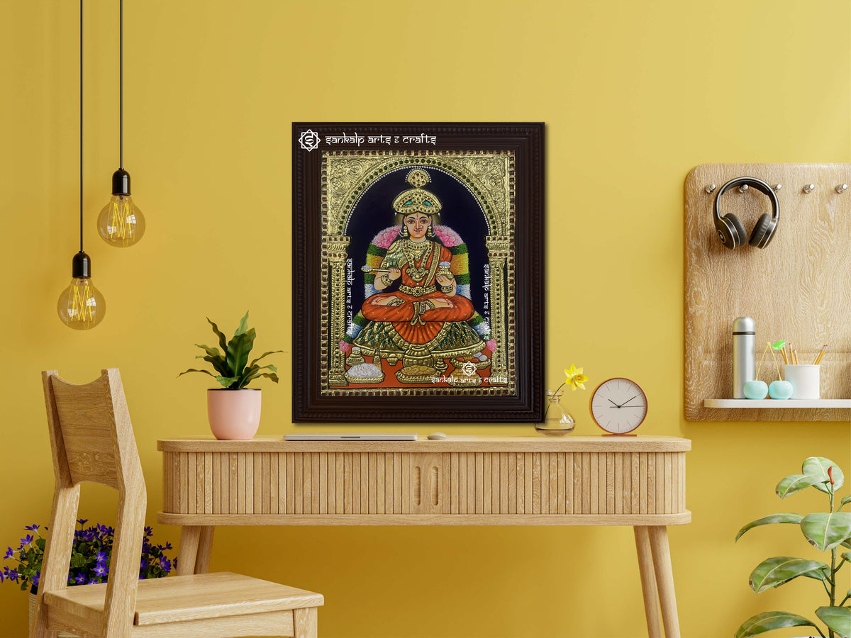 A framed Annapoorani Tanjore painting displaying the goddess in an orange saree, radiating divine grace with intricate gold work, vibrant hues, and spiritual energy.