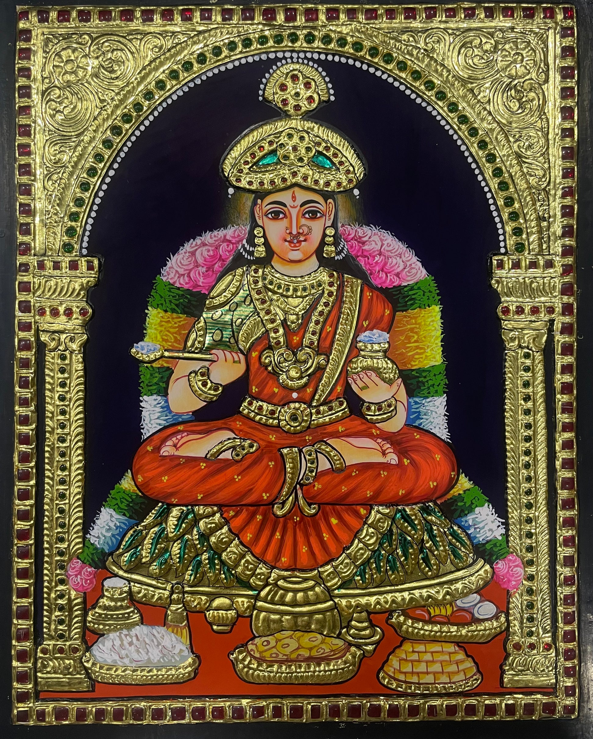 A close-up of the Annapoorani Tanjore painting, showcasing the goddess in a beautifully draped orange saree, highlighted with exquisite gold embellishments and detailed craftsmanship.


